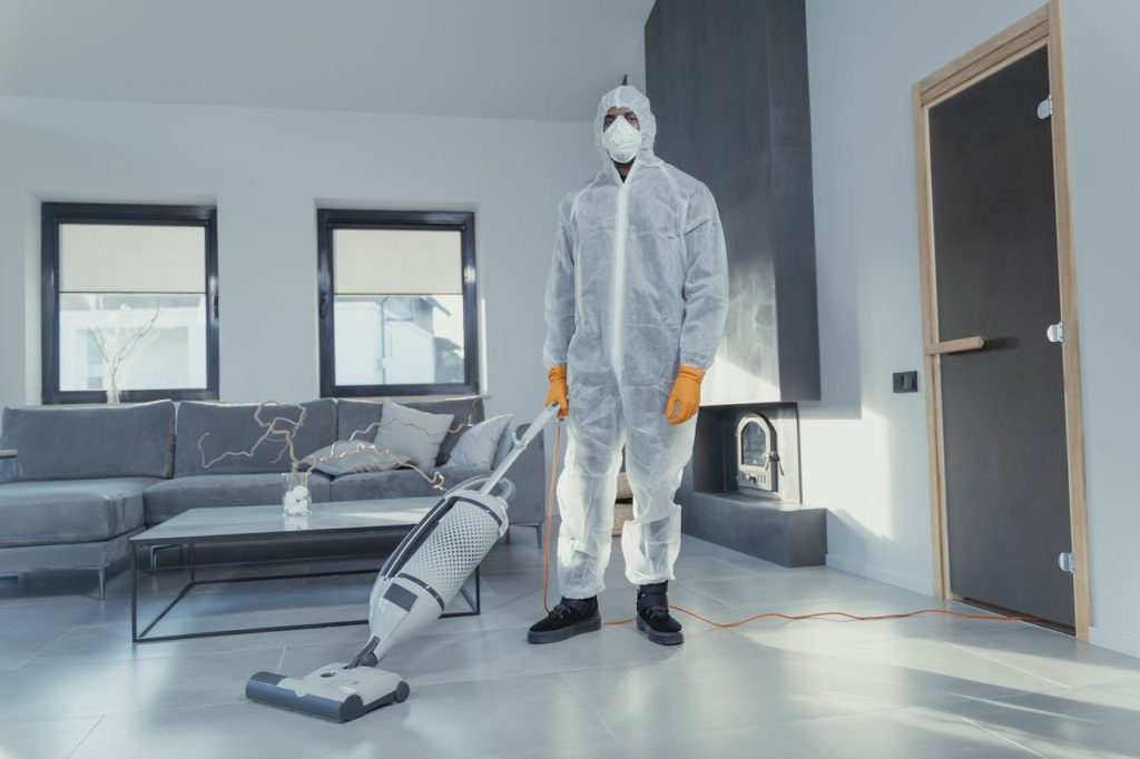 man-in-white-suit-standing-beside-white-wall-6195966 A person in protective coveralls vacuuming a contemporary living room.