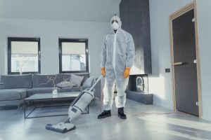 A person in protective coveralls vacuuming a contemporary living room.