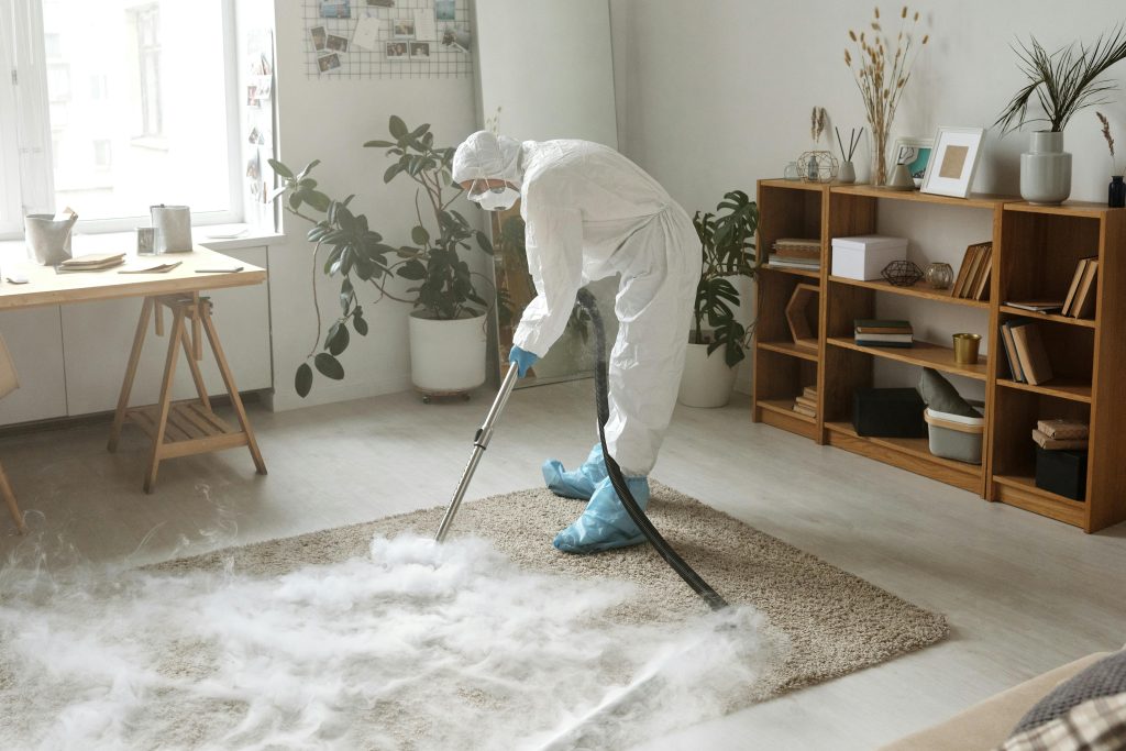 pexels-photo-4176302-4176302 A woman in protective gear disinfects a carpet indoors to ensure safety during the COVID-19 pandemic.