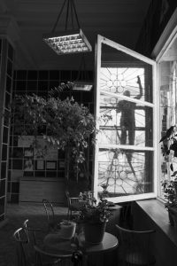 Black and white image of a worker silhouette cleaning a large decorative window in a bright interior space.